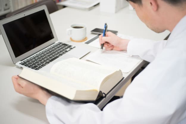 Homem sentado em frente ao computador analisando livro para tradução técnica