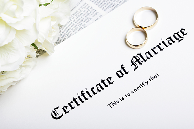 certificado dde casamento em cima de um livro ao lado de rosas brancas e um par de alianças de ouro
