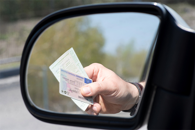 espelho retrovisor refletindo mão seurando cnh e um ticket