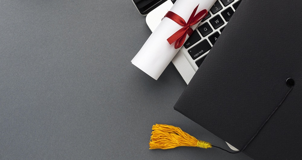 Chapéu e diploma ao lado de um notebook após ter passado por um processo de tradução juramentada de diplomas.