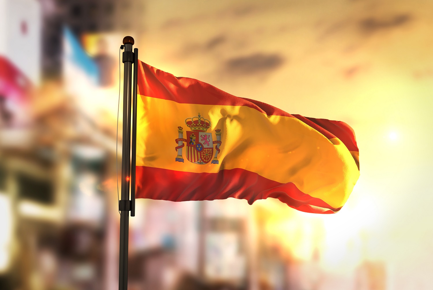 Foto da bandeira da Espanha tremulando e a cidade ao fundo em desfoque.