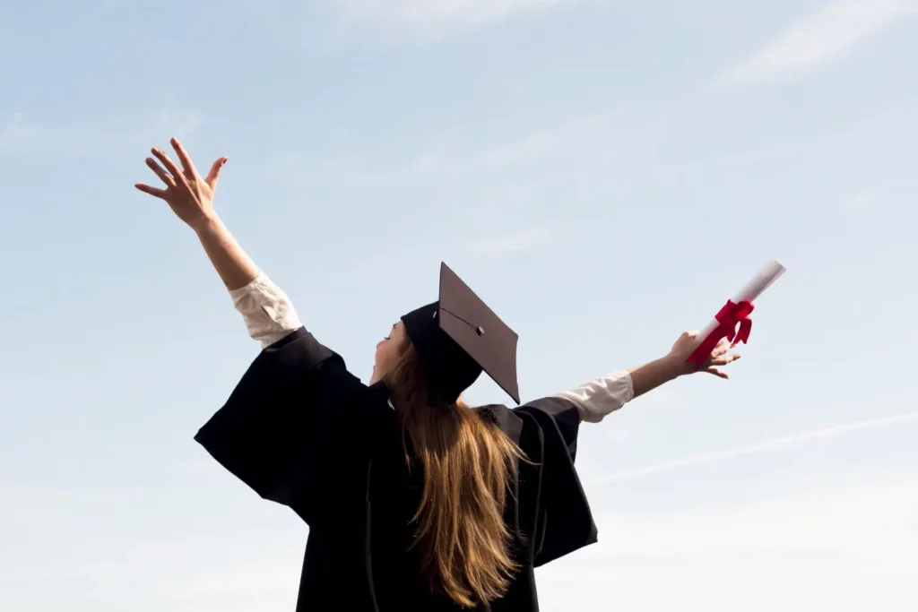 Imagem de um formando de braços abertos com capelo e seu diploma, representando a convalidação de diploma