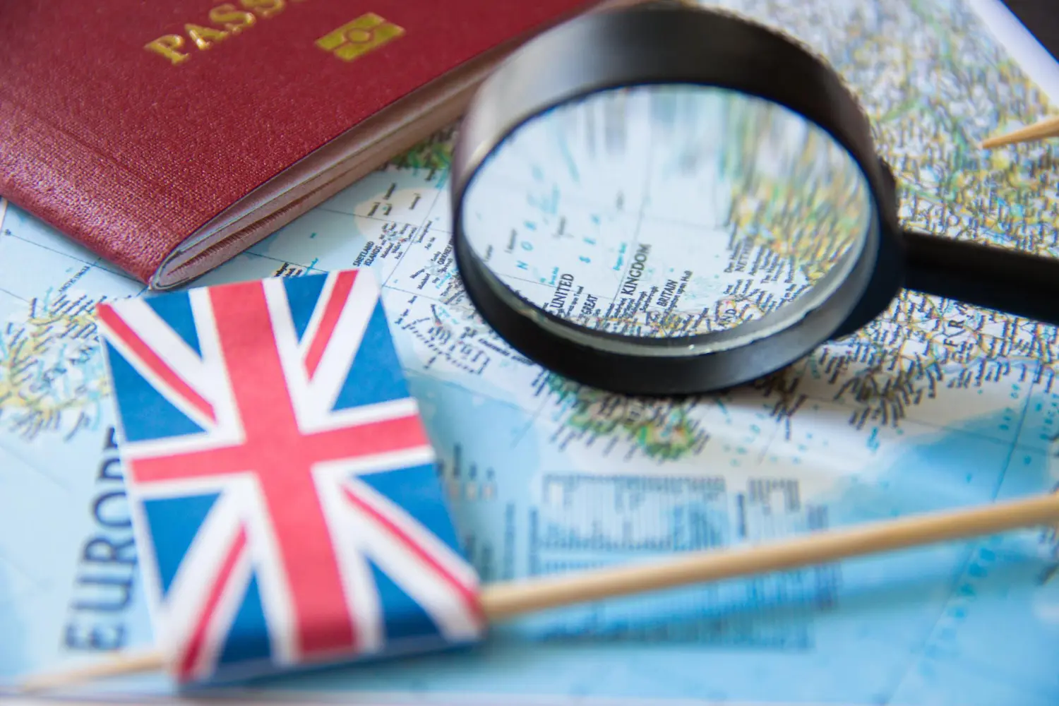 Pequena bandeira da Inglaterra, passaporte e lupa sobre um mapa para ilustrar a conquista da cidadania britânica.